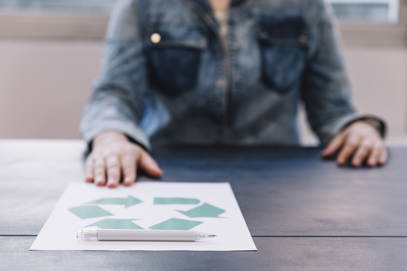 person-showing-recycle-paper-with-pen-wooden-table-1